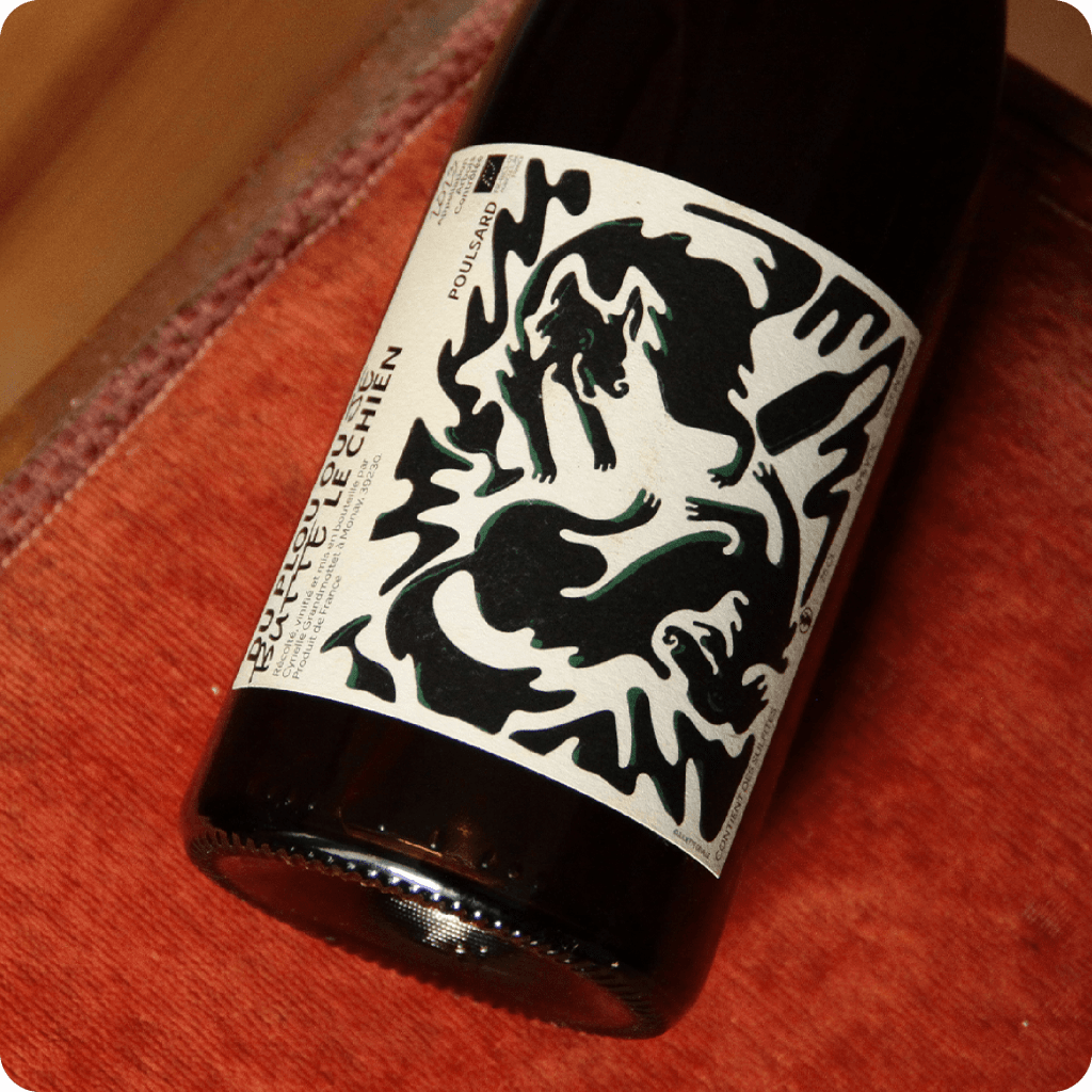 Illustration de deux chiens qui jouent en renversant des bouteilles et des verres de vin. Cette illustration se trouve sur une bouteille de vin du Jura.